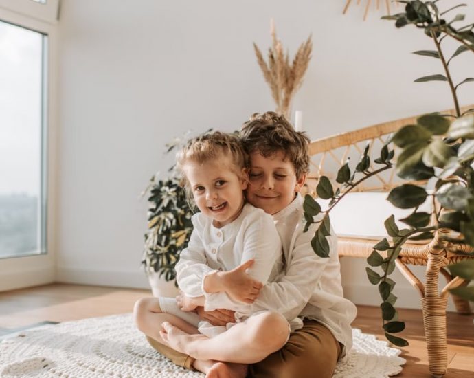 Two smiling siblings hugging in a cozy room with natural light.