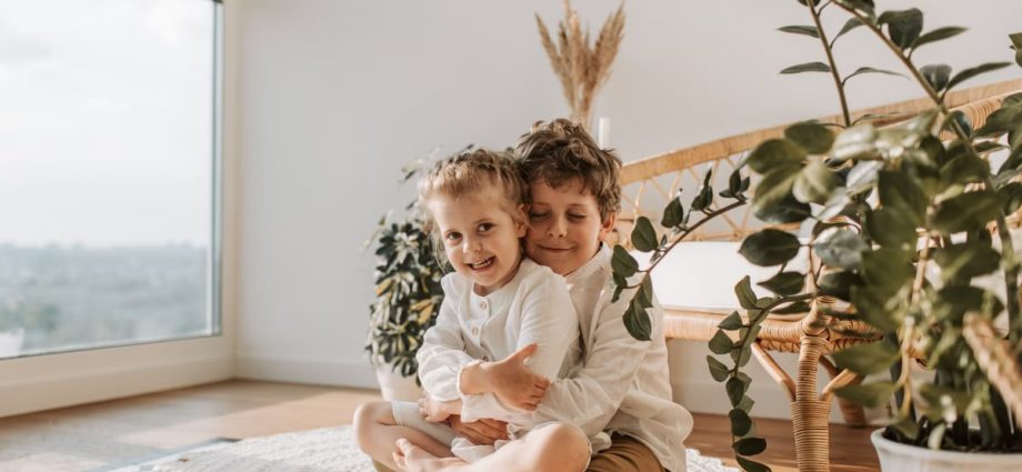 Two smiling siblings hugging in a cozy room with natural light.